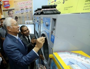 NAJIB dibantu pengasas Adan Laundry, Zamani Zakaria memasukan duit syiling ke dalam mesin basuh layan diri ketika melawat gerai pameran perniagaan francais mesin basuh layan diri Adan Laudry sempena Pameran Francais Antarabangsa Malaysia 2015 (FIM) di Pusat Dagangan Dunia Putra (PWTC), Kuala Lumpur.- Foto Aizuddin Saad 